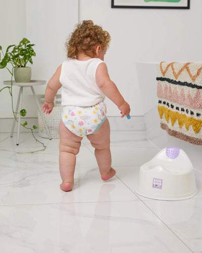 Child in a diaper standing next to a potty in a bathroom
